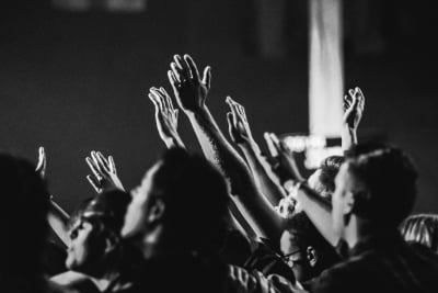 black and white image of a crowd of people with their hands raised in worship